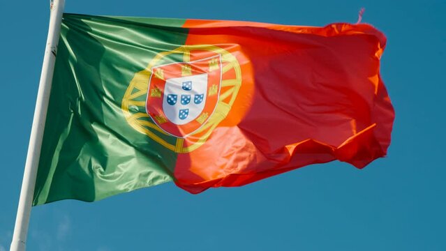 Slow motion close-up view of the flag of Portugal flying against a blue sky background