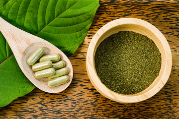 Mitragyna speciosa (kratom) leaves with medicinal products in capsules. and the powder in the wooden cup with the wood texture as the background