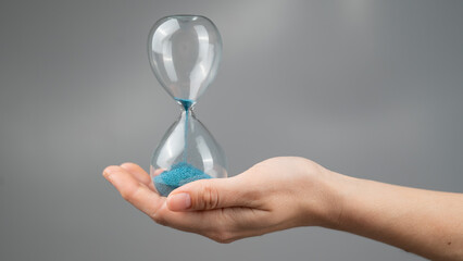 Woman holding an hourglass on a gray background. Close-up.