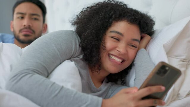 Couple in bed, infidelity, and woman with phone, smile and secret affair with man checking over shoulder. Smartphone, technology and social media, wife cheating online with worried husband in bedroom