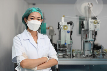 Worker in personal protective equipment or PPE inspection quality crossed arms and looking camera in mask and medical face mask production line factory, manufacturing industry and factory concept.