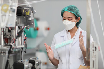 Fototapeta na wymiar Worker woman in personal protective equipment or PPE inspecting quality of mask and medical face mask production line in factory, manufacturing industry and factory concept.