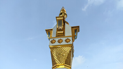 Replica of the columns of the An-Nabawi Mosque against the background of a clear sky. Islamic cultural art with gold color. Photographed from below facing left.