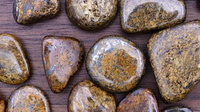 Bronzite heap up jewel stones on brown varnished wood texture. Moving right seamless loop backdrop.
