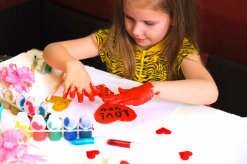 Child making homemade greeting card. A little girl paints a hearts as a gift for Mother’s Day or VAlentines day. Traditional play concept. Arts and crafts concept. - obrazy, fototapety, plakaty