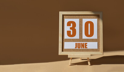 June 30th. Day 30 of month, Calendar date. Cork board, easel in sunlight on desktop. Close-up, brown background. Summer month, day of year concept