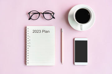 Flat lay of mobile phone, a cup of coffee, glasses and notepad of businesswoman on pink table in...