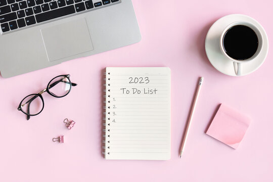Flat lay of computer, a cup of coffee, glasses and office stationary of businesswoman on pink desk in office. Business and technology, to-do list on 2023. Top view and copy space for text