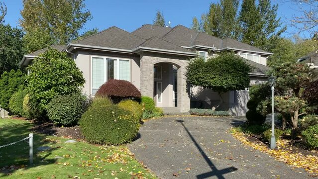 Establishing shot of two story stucco luxury house with garage door, big tree and nice Fall Foliage landscape in Vancouver, Canada, North America. Day time on Sept 2022. ProRes 422 HQ.