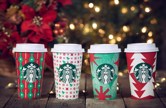 A row of Starbucks coffee beverages in the new 2022 designed holiday cups, in Dallas, Texas, on November 6, 2022. Displayed on wooden table against festive Christmas light bokeh background.