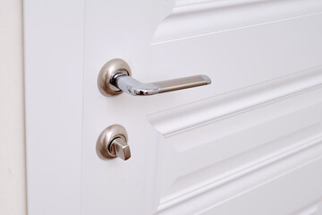 A white door with a lock in the home room and a light switch. Metal door handle in the apartment