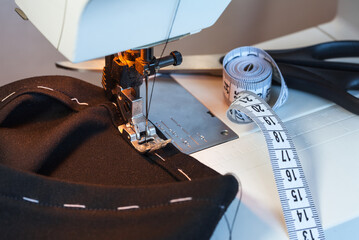 Sewing clothes at home as a hobby. Processing the bottom of black trousers on a basting with white...
