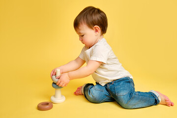 Toddler baby is playing logic educational games with a pyramid on a studio yellow background. Happy...