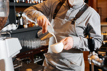 Close-up of a masked bartista preparing delicious delicious coffee at the bar in a coffee shop. The work of restaurants and cafes during the pandemic.
