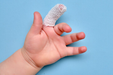 Baby s hand with a bandaged finger on a blue studio background, close-up. Injured index finger of a child wrapped in a white bandage. Kid boy aged one year and three months