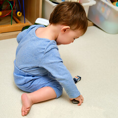 Toddler baby boy is playing with toy cars on the floor in the home room. A child plays with toys in...