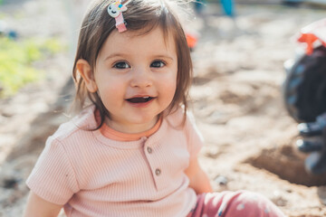 Portrait of a cute baby girl playing in sand on outdoor playground, having fun on warm summer day....