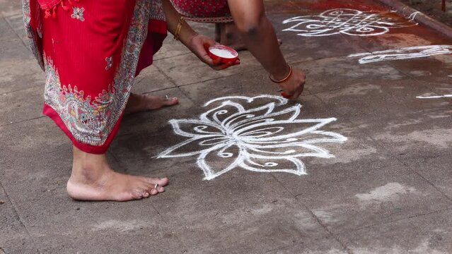Indian women putting kolam Rangoli in front of Indian Temple for Pongal dedicated to the Hindu deity ancient texts of the Puranas. Dravidian vintage architecture in Tamilnadu India 4k video footage.