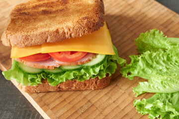 A delicious cheese and vegetable sandwich, close-up on a wooden background.