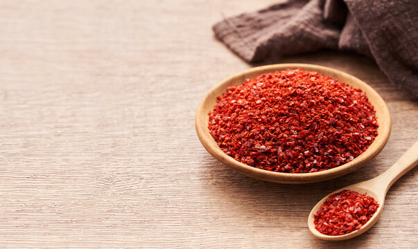 close up a pile of red pepper flake or heap of red pepper powder coarse. korean chili ground Gochugaru in white bowl and wood spoon on wooden table background                             