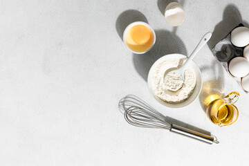 Baking ingredients: flour, eggs, whisk, butter and milk on a white concrete background. Baking concept.