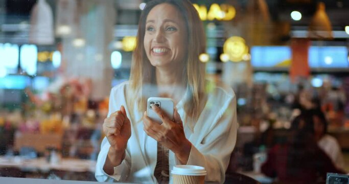 Caucasian pretty woman using smartphone, scrolling news feed and checking social media content, clenching fists from happiness, expressing surprised emotion from good news