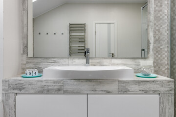 Bathroom with a shower cabin, a large mirror and a chrome heater or a radiator of a towel against a white wall. Loft style in a new apartment
