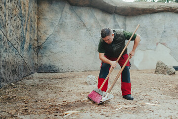 Caretaker with down syndrome in zoo cleaning animal enclosure. Concept of integration people with...