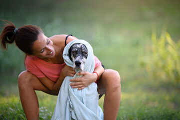Adult woman wrapping her dog with a towel after a bath in the garden. Pet care concept.