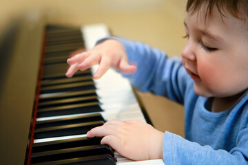 Toddler baby plays piano in home living room, music lessons. Happy child boy learns to play music...