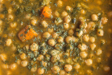 Overhead view of a closeup detail of a cooked dish of chickpeas with spinach parsley and carrot. Organic texture abstract background.