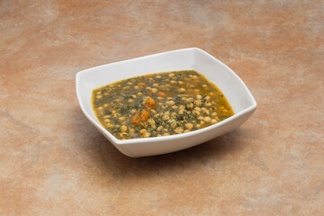 An elegant deep geometric white ceramic dish with a stew of chickpeas with spinach on a natural stone countertop..Food and legumes.