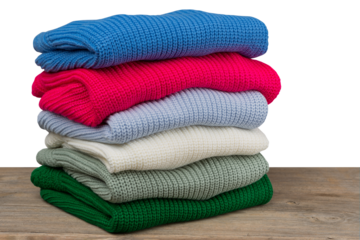 Six knitted sweaters of different colors are folded and lie in a pile one on top of the other, on wooden boards.