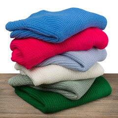Six knitted sweaters of different colors are folded and lie on a wooden table in a pile one on top...