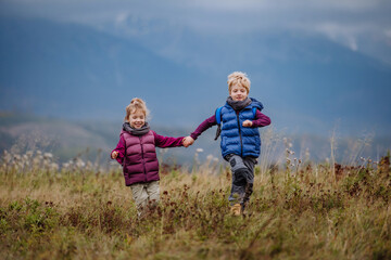 Little children holding each other hands and runing at autumn meadow.