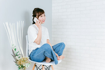 家で椅子に座りながらスマホを使うアジア人女性  © buritora