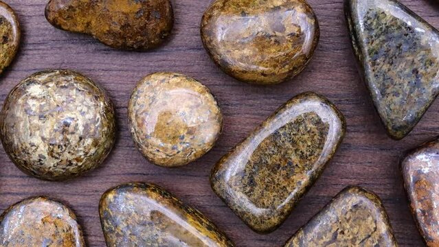 Bronzite rare jewel stones on brown varnished wood texture. Moving right seamless loop backdrop.