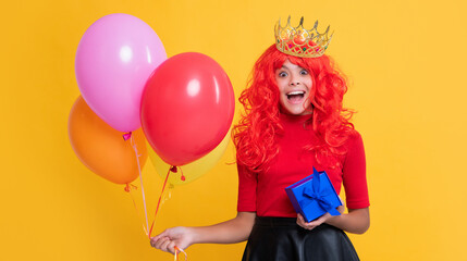 shocked child in crown with present and party balloon on yellow background