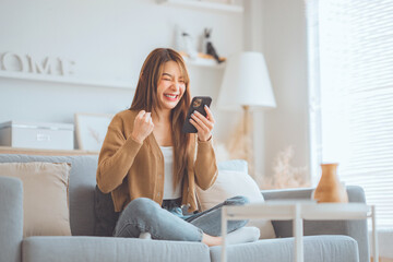 Excited young asian woman hold phone chatting in dating app feel happy sit on sofa at home, Closeup...