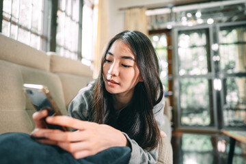 Young adult asian woman relax lying using smartphone for counseling or therapy at home sofa - obrazy, fototapety, plakaty