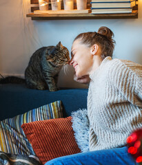 A cute gray tabby cat licks the nose of a happy young owner woman. Love and care for pets