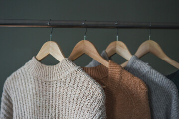 Warm cozy sweaters in neutral gray and beige shades hanging on hangers