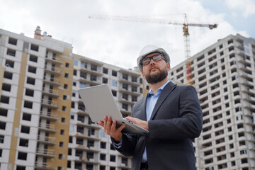 Bearded building inspector making notes on laptop at construction site