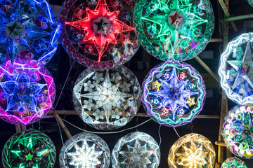 Brightly colored Parols for sale at a stand at nighttime. A Filipino ornamental lantern displayed...