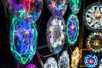 Brightly colored Parols for sale at a stand at nighttime. A Filipino ornamental lantern displayed...