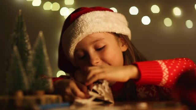 child unfolds paper snowflake with delight against backdrop of Christmas decorations in evening. craft for kids.