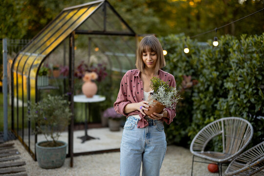 Woman with flowerpot in garden with greenhouse behind
