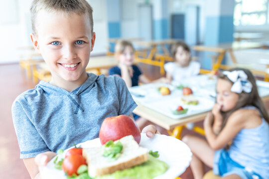 Smiling boy holding healthy lunch on plate standing at cafeteria