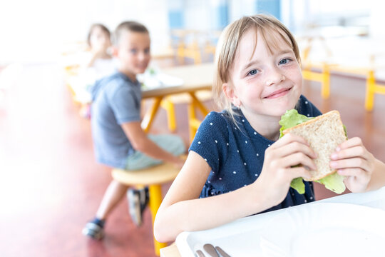 Smiling student holding sandwich at lunch break in cafeteria