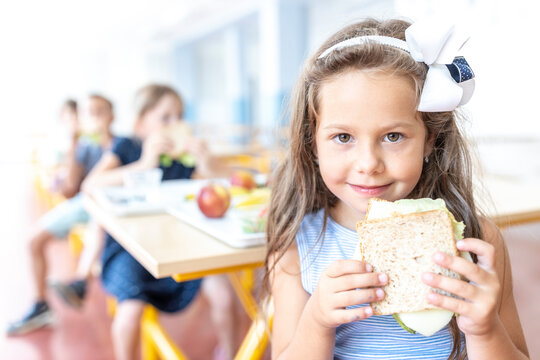 Girl wearing headband holding sandwich at lunch break in cafeteria
